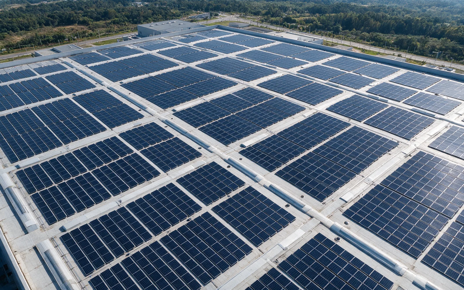 Aerial view of a factory roof fully covered in dark photovoltaic arrays with pale concrete maintenance walkways between them.